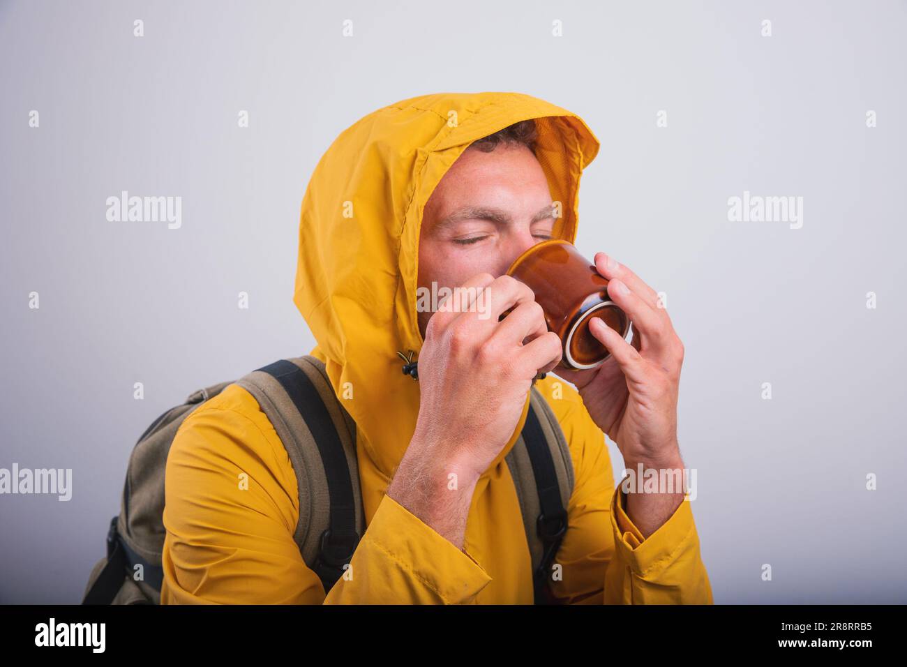 A man drinks healthy herbal tea while wearing a raincoat Stock Photo