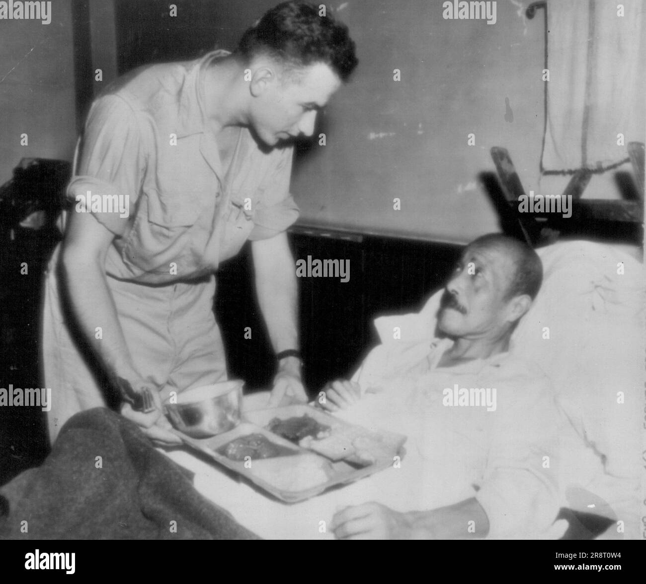 Former Premier of Japan Recovering -- Former premier of Japan, general Hideki Tojo, receives a tray of GI food at the U.S. 43rd field hospital, Yokohama, where he is recovering from self-in-flicted bullet wound suffered in his attempted suicide Sept. 11, 1945. Corp Edwin J. Podosek, hospital orderly of Chicago, Ill., serves the meal. October 16, 1945. (Photo by AP Wirephoto). Stock Photo