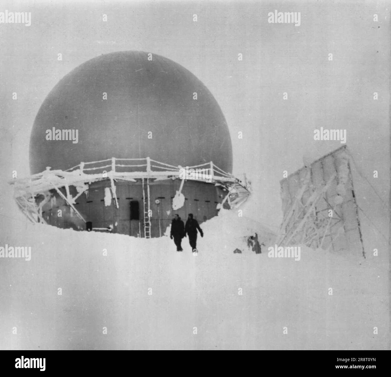 Arctic Eye -- This huge dome, like a small observatory, is typical of many radar outposts that dot our northland, overlooking the Bering Sea, with a watchful eye to give first alarm in case enemy bombers might come toward U.S. Fence-like structure at right is radio antenea. Air Force men in foreground show size of structure. February 02, 1955. (Photo by AP Wirephoto). Stock Photo