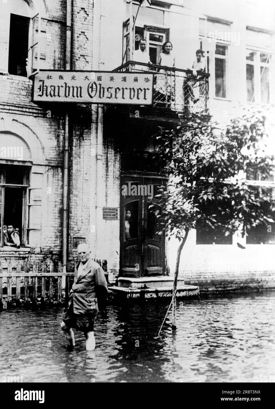 Floods In Harbin, Manchuria -- The offices of the 'Harbin Observer', the only British owned and British edited paper in Manchuria, showing the proprietor and editor, Mr. B. Hayton Fleet wading through the floods to the printing house. The flood water stood at the same level for ten days and the Chinese unconcernedly washed their linen at their doors whilst the stench in the streets from dead rats and other reuse was unbearable. October 24, 1932. (Photo by Sport & General Press Agency Limited). Stock Photo