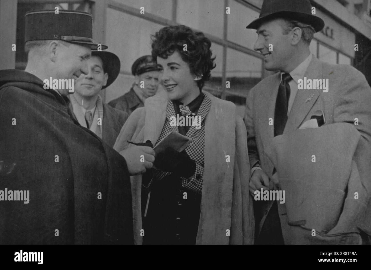 Elizabeth Taylor On Her Honeymoon - Elizabeth Taylor and Michael Wilding on their arrival at le bourget. They are giving their autographs to a policeman. Elizabeth Taylor and Michael Wilding who were married last Thursday called at Paris on their honeymoon. The new Mrs. Wilding is 19 and her husband 39. February 25, 1952. (Photo by Paul Popper, Paul Popper Ltd.). Stock Photo