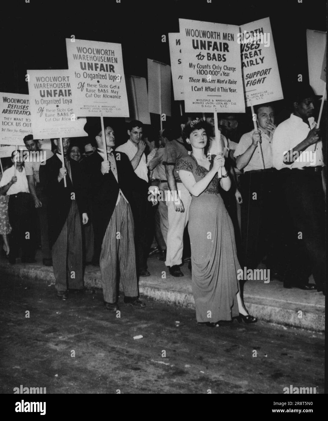 'Babs Hutton' Take off By Woolworth Pickets -- Woolworth warehouse employees and members of local 65, wholesale and warehouse union, picket the Woolworth Building in New York City, June 30, demanding re-signing of the union contract. The girl in evening gown is doing a takeoff on heiress 'Babs' and men in striped, trousers and frock coats picket the pickets. July 22, 1947. (Photo by Associated Press Photo). Stock Photo