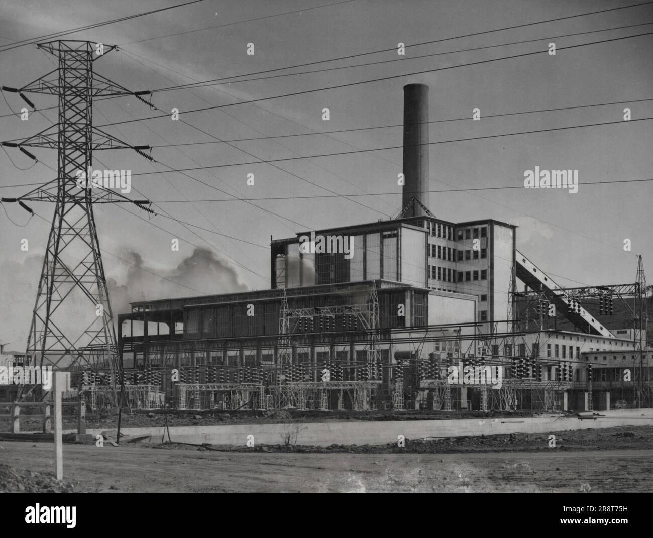 Tallawarra Power Station from the north-east frontage to Lake Illawarra with the switchyard in front and 132 kV transmission line and steel tower. October 26, 1954. Stock Photo