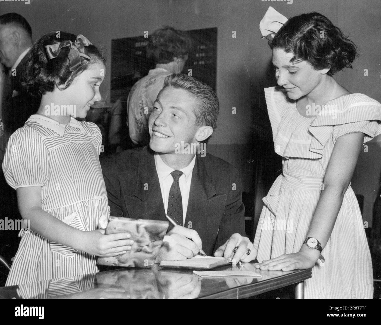 US Tennis team leaves -- US Tennis player Tony Trabert signs autographs for Kathryn (left) and Diane Humphrey before leaving for the United States with the Davis cup team this morning. Kathryn and Diane are the daughters of Ted Humphrey, the man who offered Sedgeman £40,000 to turn professional. January 02, 1952. (Photo by Stuart William MacGladrie/Fairfax Media). Stock Photo