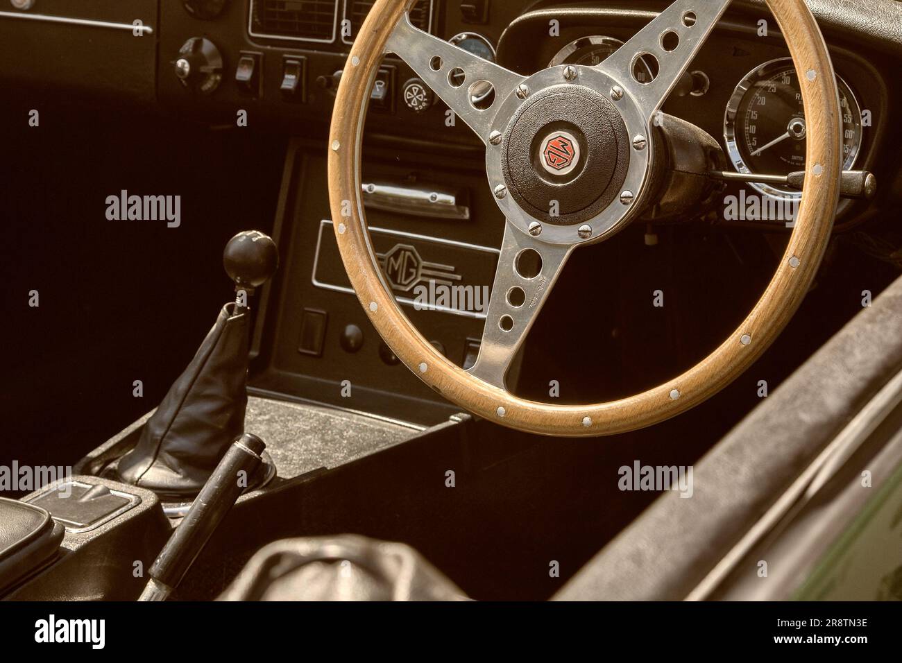 The interior of a 1970s MGB Roadster, showing the MG logo, dashboard and wooden steering wheel. British sports car at a classic and vintage car show. Stock Photo