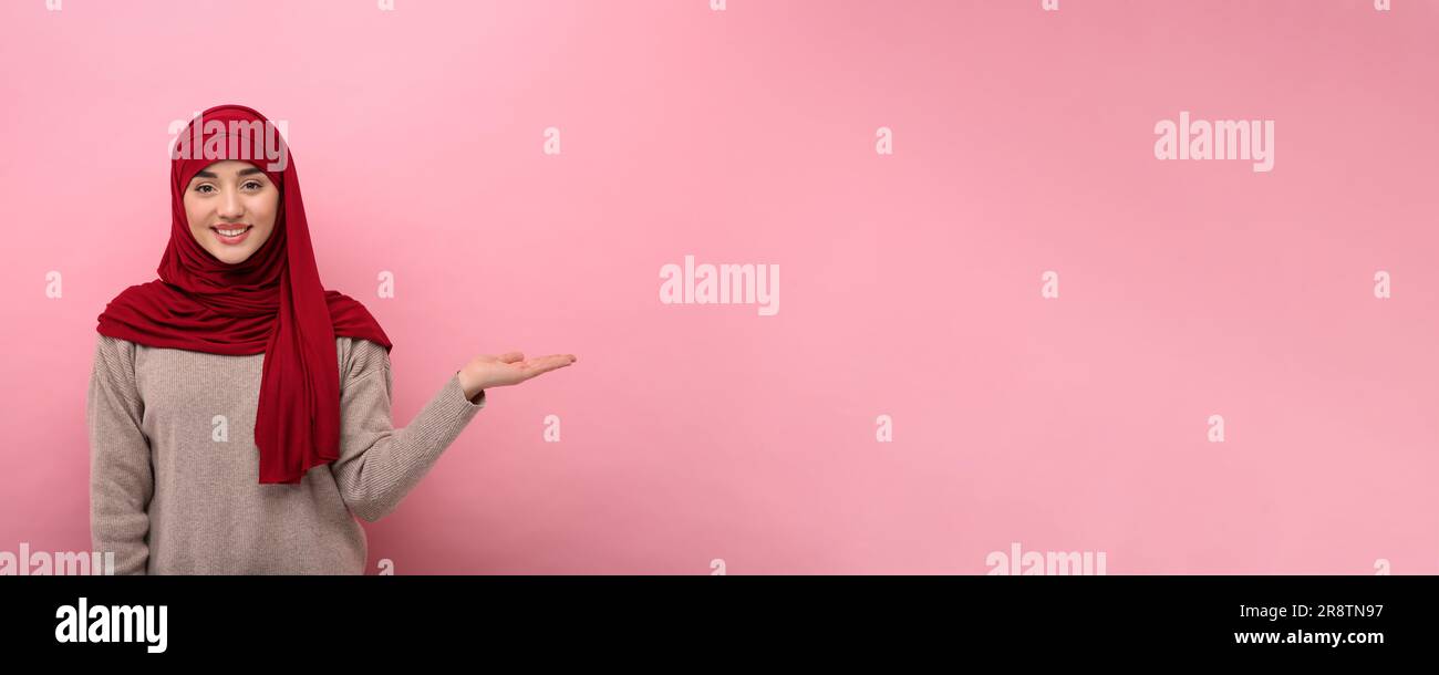 Muslim woman in hijab pointing at something on pink background, space ...