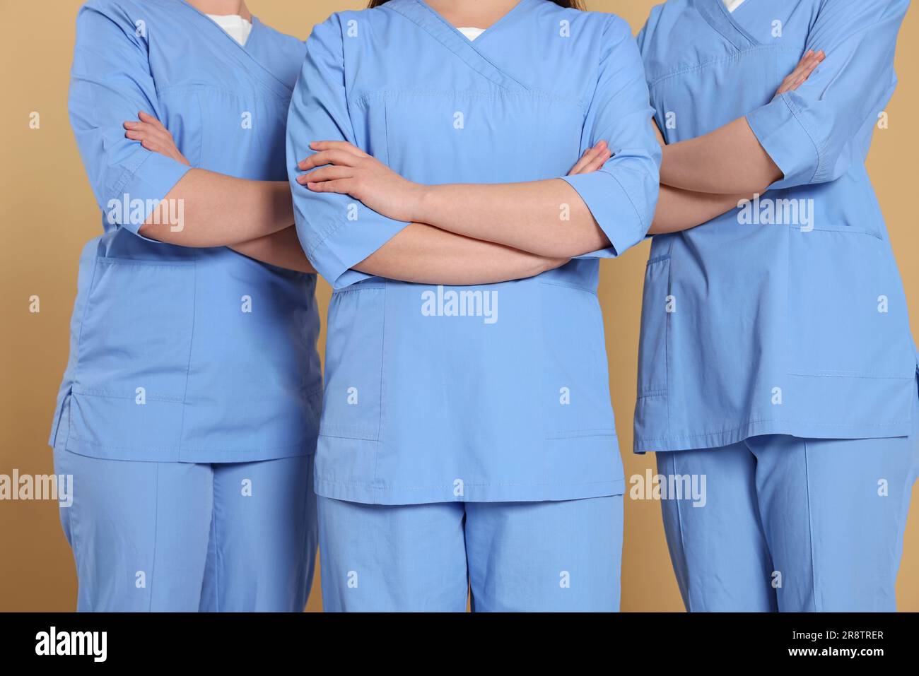 Nurses in medical uniforms on light brown background, closeup Stock