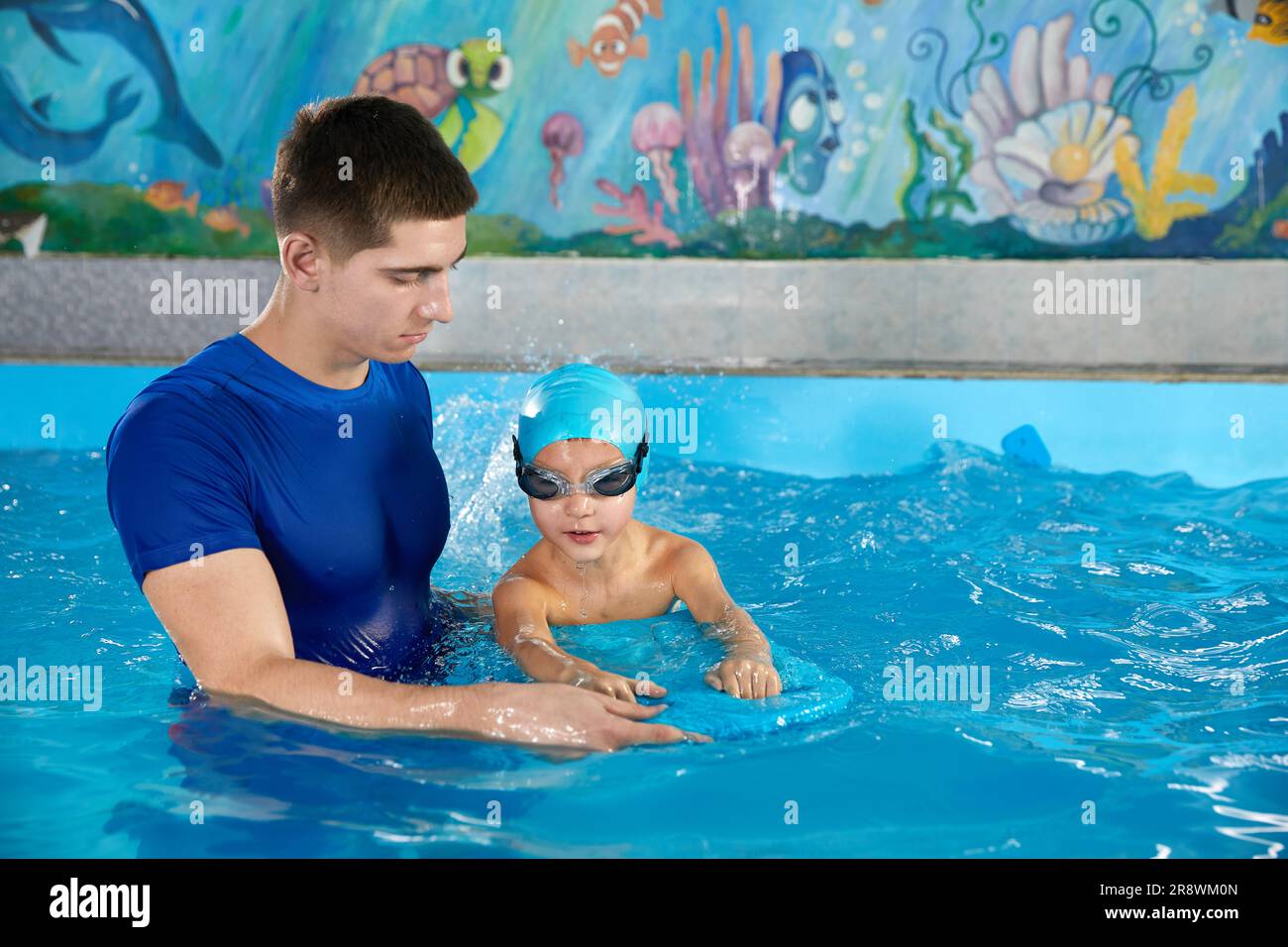 Trainer teaching little boy how to swim in indoor pool with pool