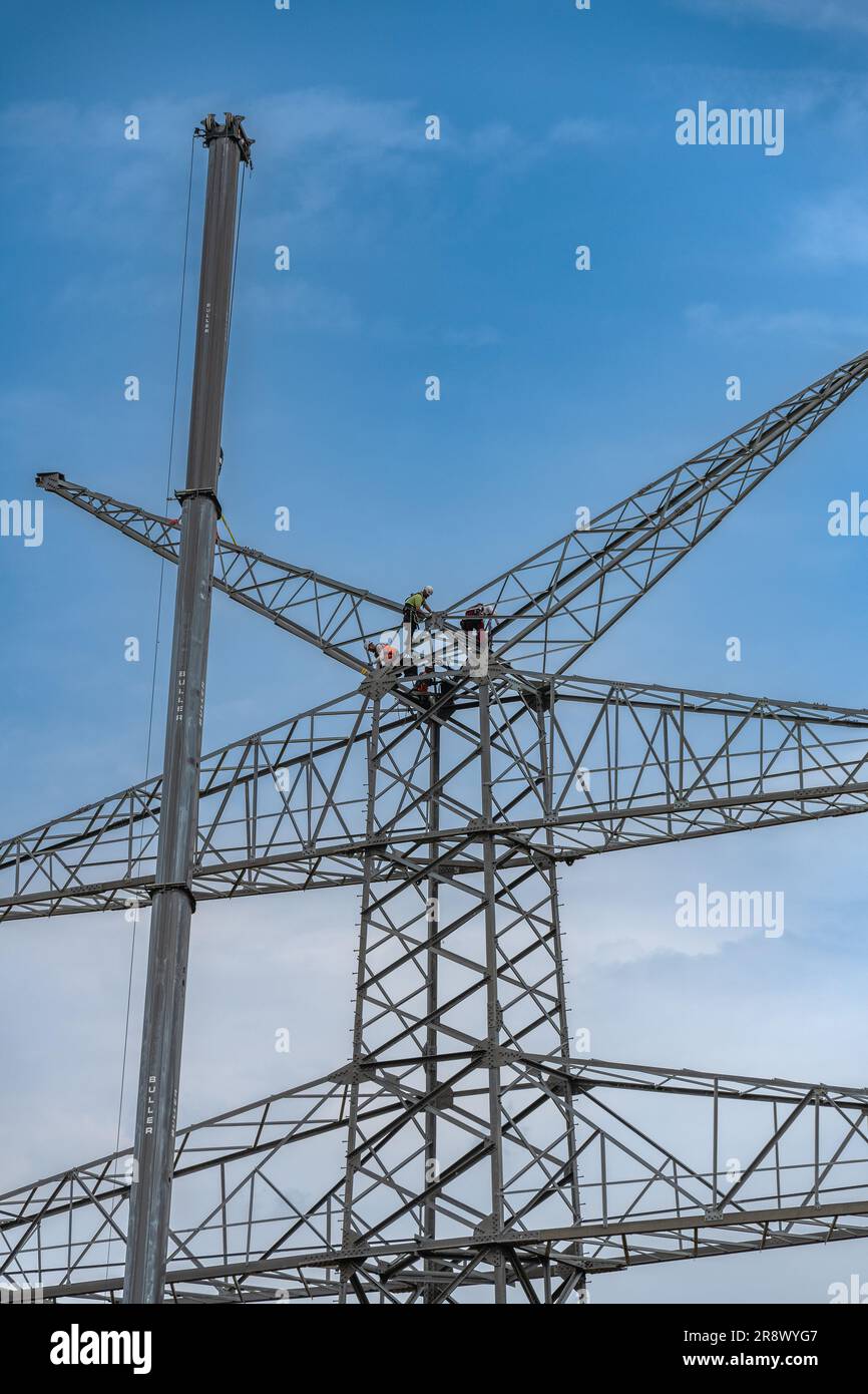 workers assembling a power pole at high altitude Stock Photo