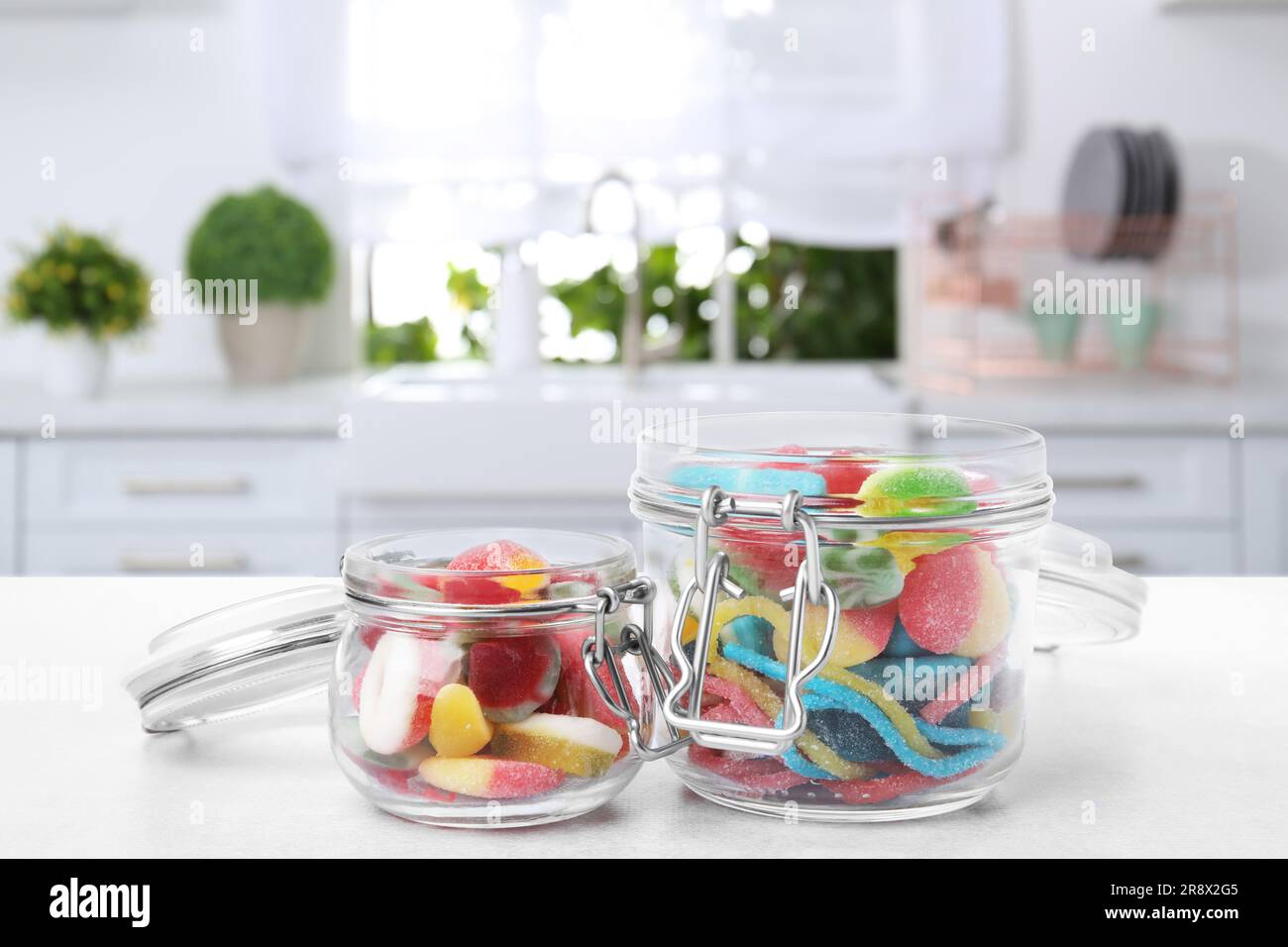 Glass jars with tasty gummy candies on white table in kitchen. Space
