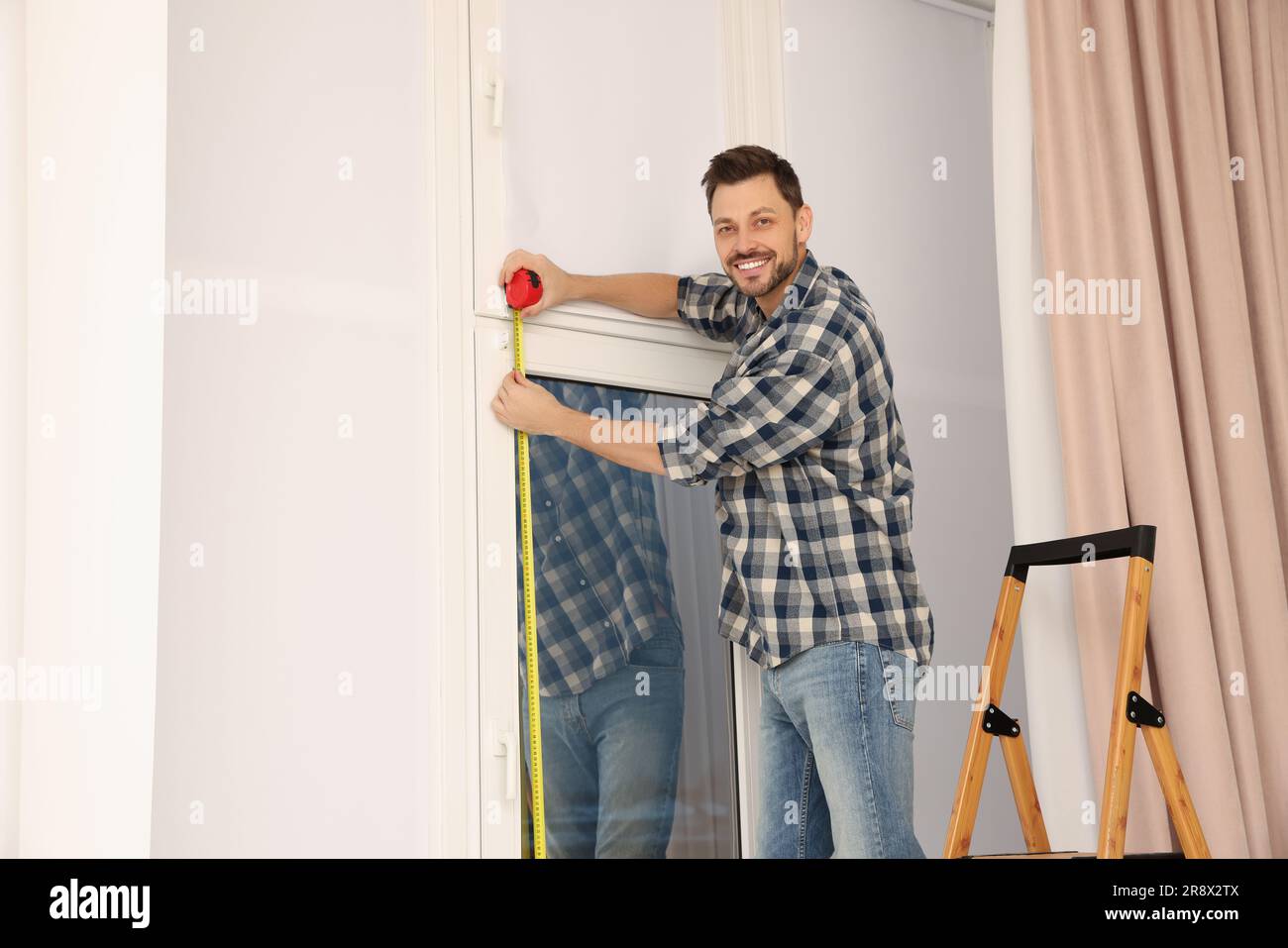 Man measuring window with tape indoors. Roller blinds installation Stock Photo