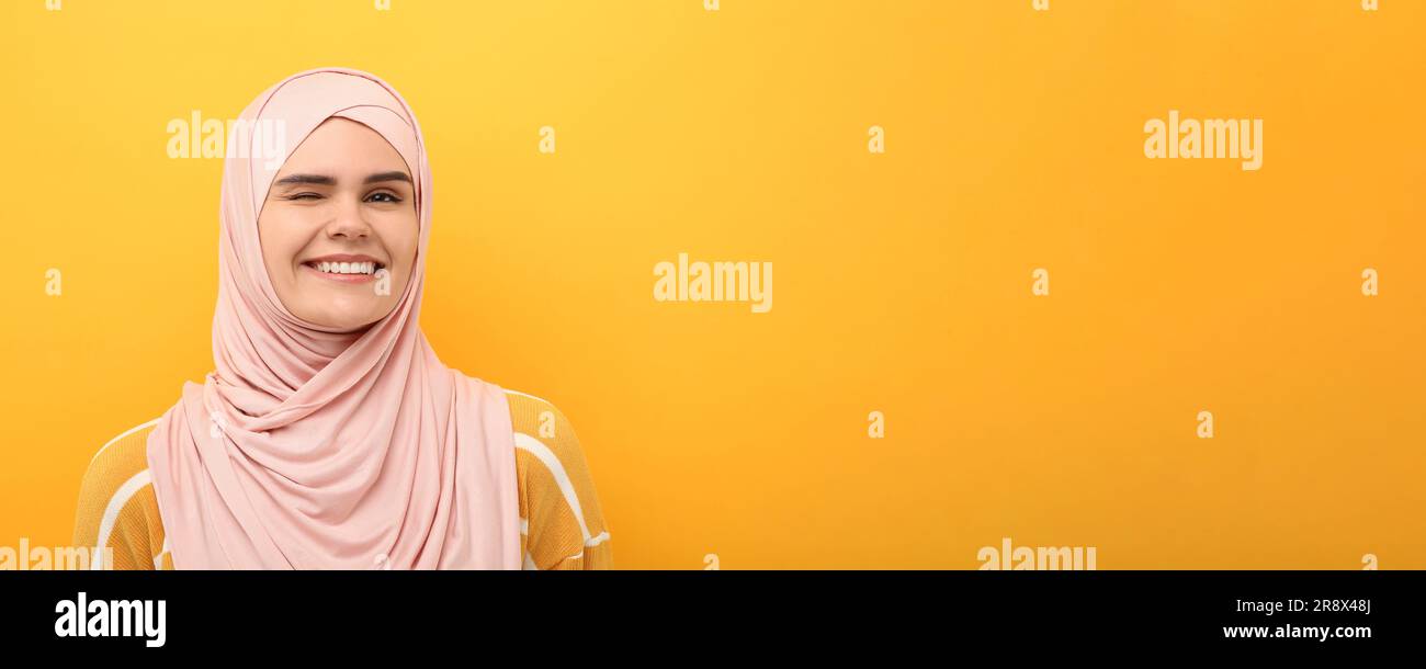 Portrait of Muslim woman in hijab winking on yellow background, space ...