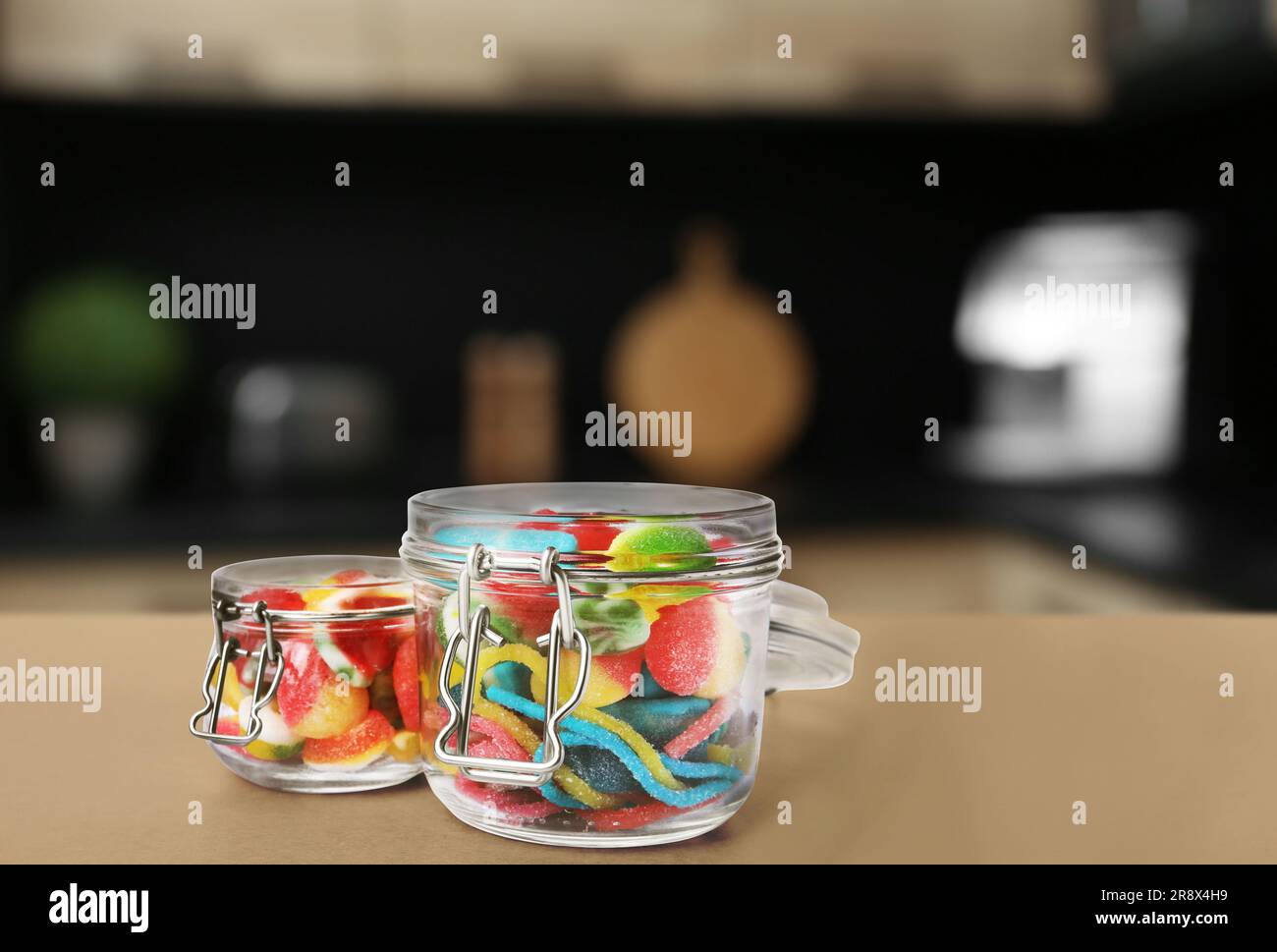 Glass jars with tasty gummy candies on light brown table in kitchen
