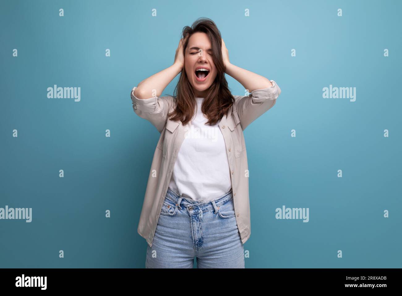 young dark-haired lady in informal clothes screaming on a blue background Stock Photo