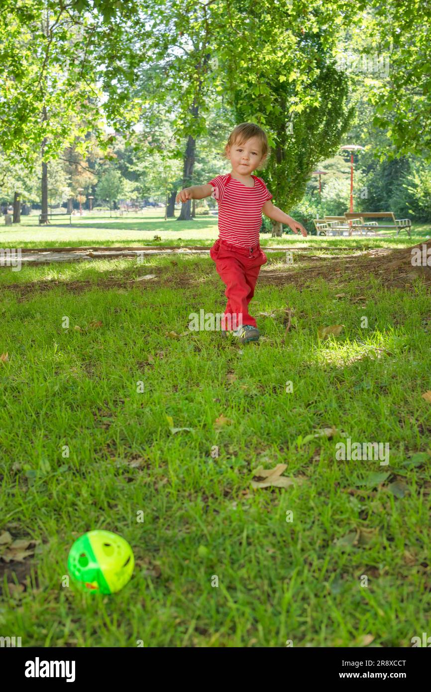 Happy little child having fun playing with his toy ball in the park ...