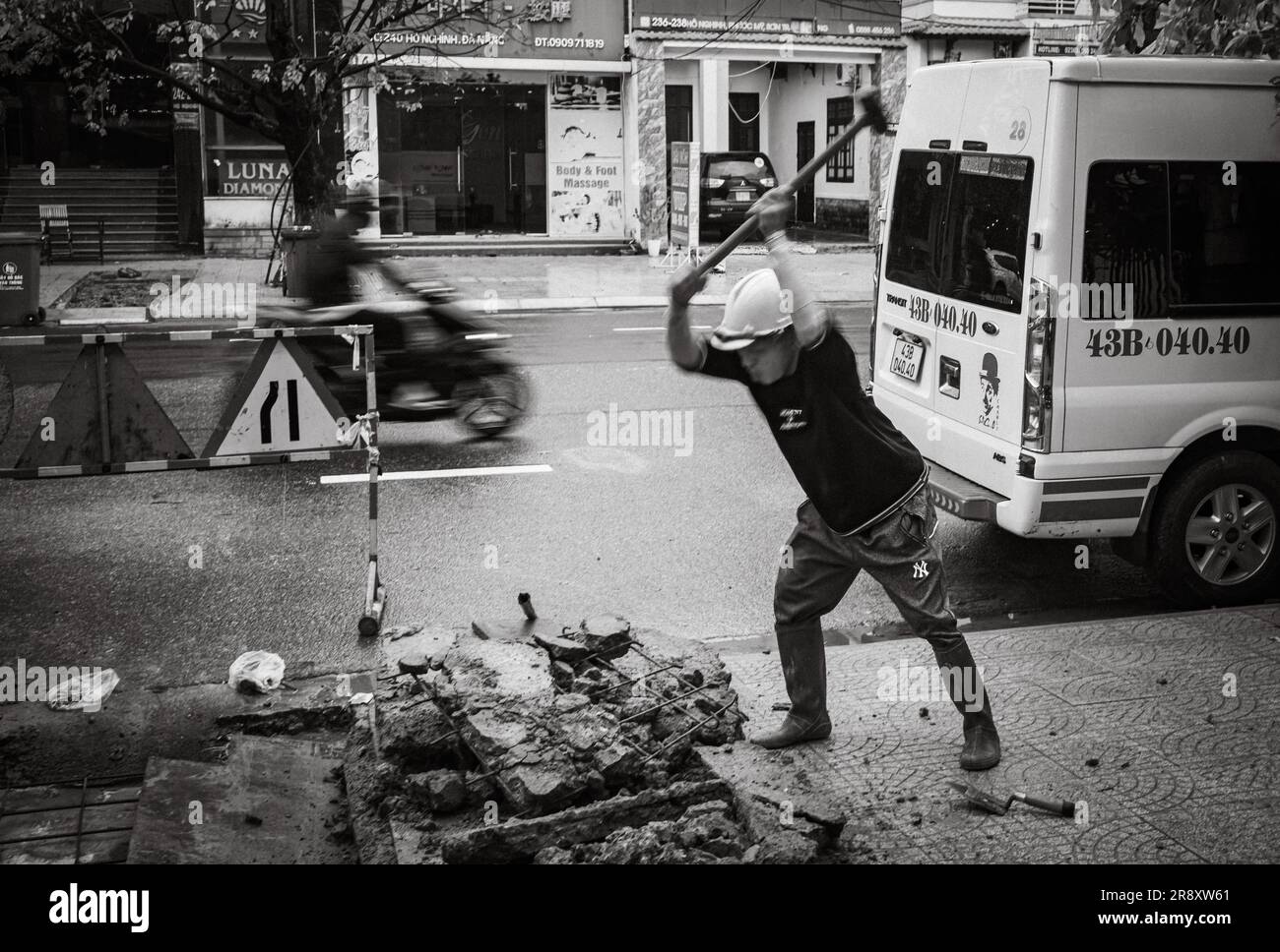 A worker smashes concrete with a sledgehammer on the pavement in Danang, Vietnam. Stock Photo