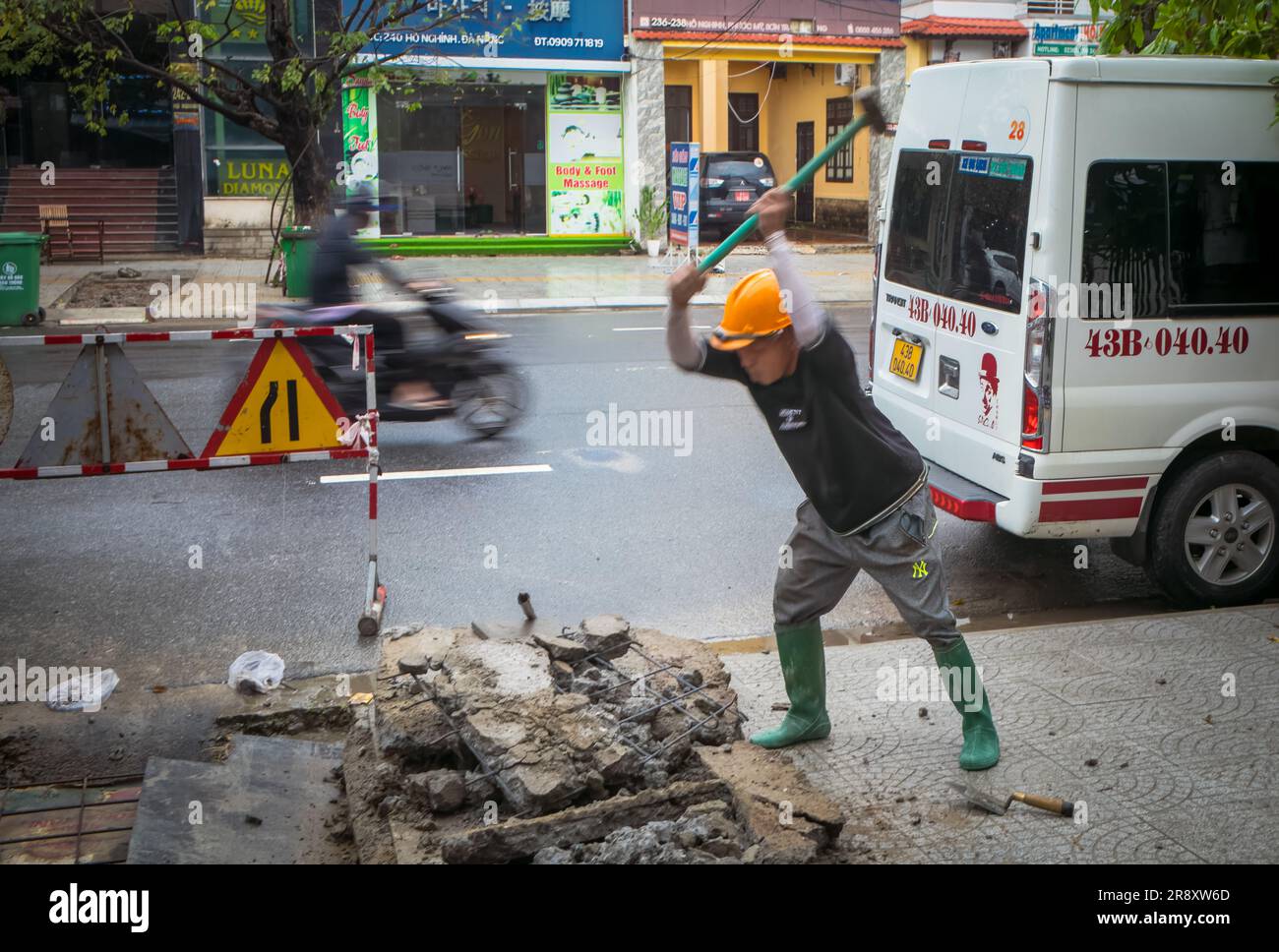 A worker smashes concrete with a sledgehammer on the pavement in Danang, Vietnam. Stock Photo