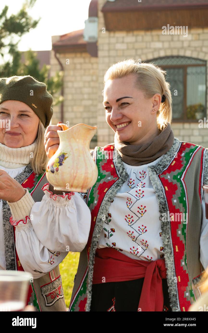 Bender, Transnistria, Moldova - November 11, 2022: Smiling woman in national Moldovan costume with a jug of wine at the wine fair on a sunny November Stock Photo