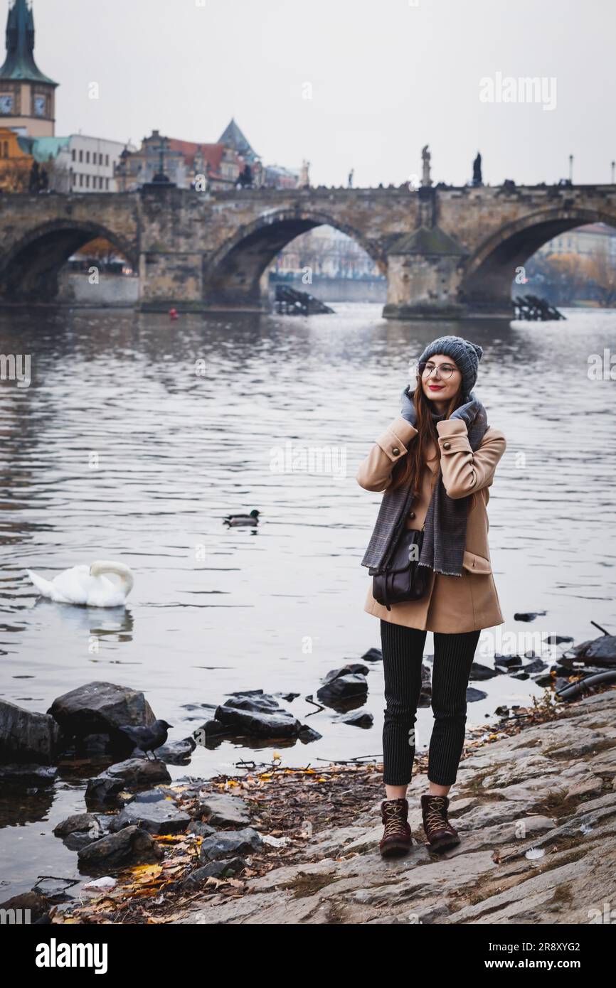 woman in a coat on bank of Vltava near Charles Bridge in Prague Stock Photo