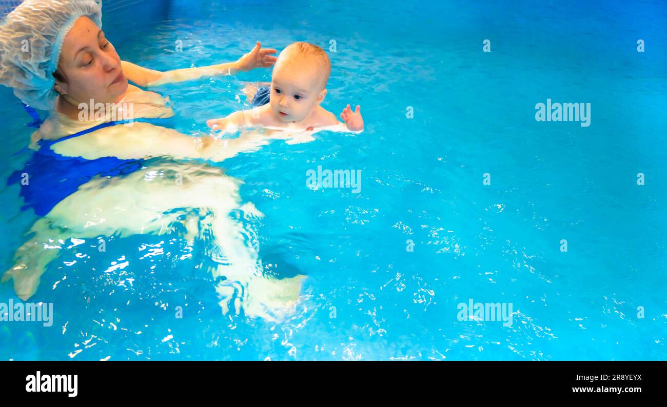 Adorable baby girl enjoying swimming in a pool with her mother early