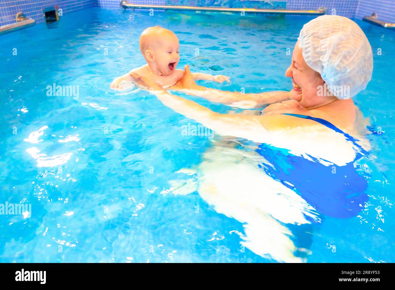 Adorable baby girl enjoying swimming in a pool with her mother early