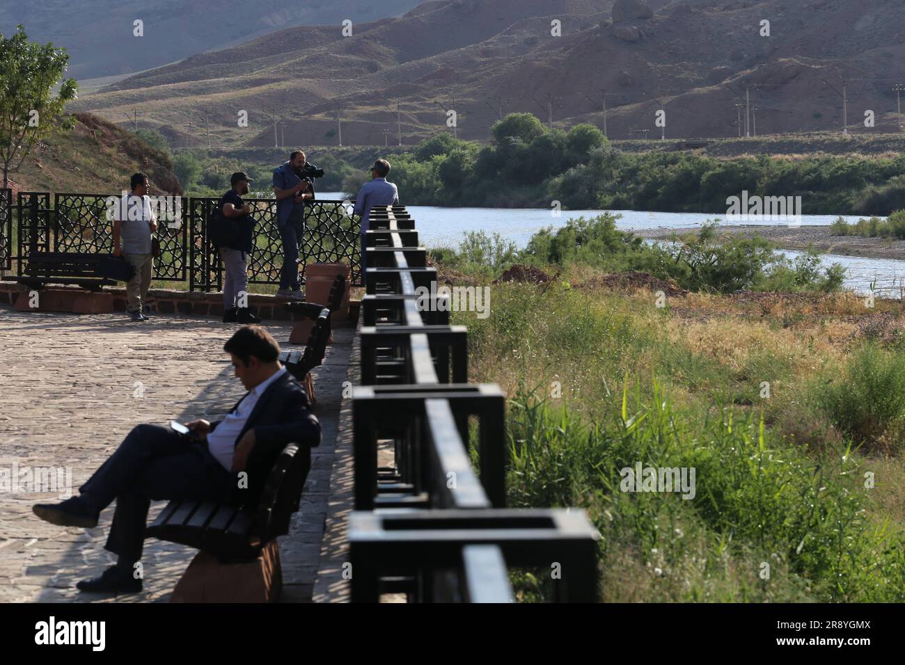 June 21, 2023, Jolfa, East Azerbaijan, Iran: People stand near the Aras River at the border between northwestern Iran and Azerbaijan. The Aras (the Araks, Arax, Araxes, or Araz) is a river in the Caucasus. It rises in eastern Turkey and flows along the borders between Turkey and Armenia, between Turkey and the Nakhchivan exclave of Azerbaijan, between Iran and both Azerbaijan and Armenia, and, finally, through Azerbaijan where it flows into the Kura River. It drains the south side of the Lesser Caucasus Mountains while the Kura drains the north side of the Lesser Caucasus. The river's total le Stock Photo