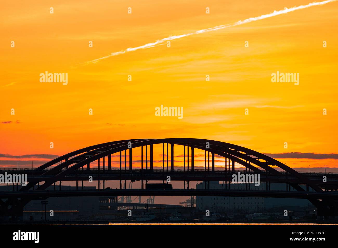 A vivid orange dawn sky behind the silhouette of the doubledeck arched Kobe Bridge connecting