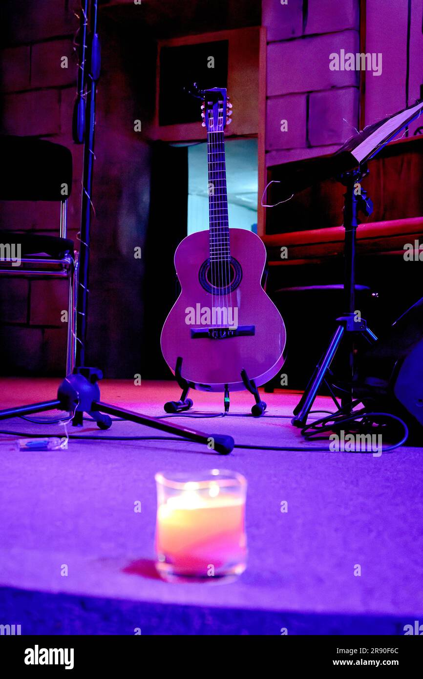 An image of an acoustic guitar stands on stage near a music stand Stock