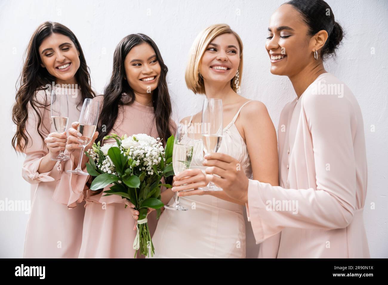 positivity, blonde bride in wedding dress holding bouquet, standing with  interracial bridesmaids, champagne glasses, grey background, racial  diversity Stock Photo - Alamy