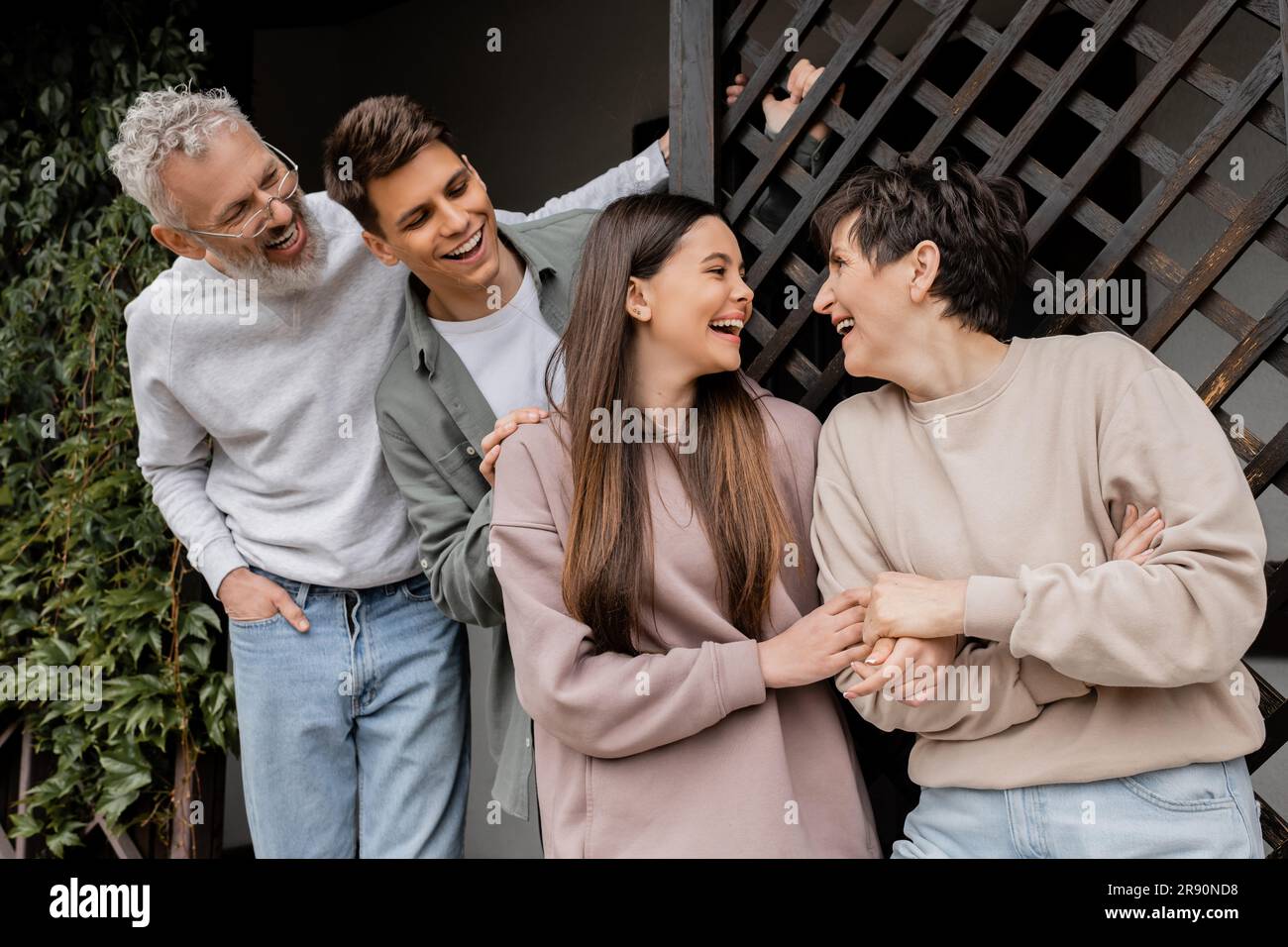 Joyful teenage girl holding hand of middle aged mother near family