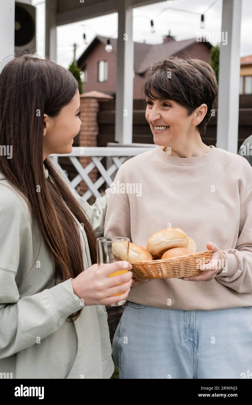 modern parenting, celebration of parents day, happy middle aged mother holding buns and talking with her teenage daughter, modern parenting, suburban Stock Photo