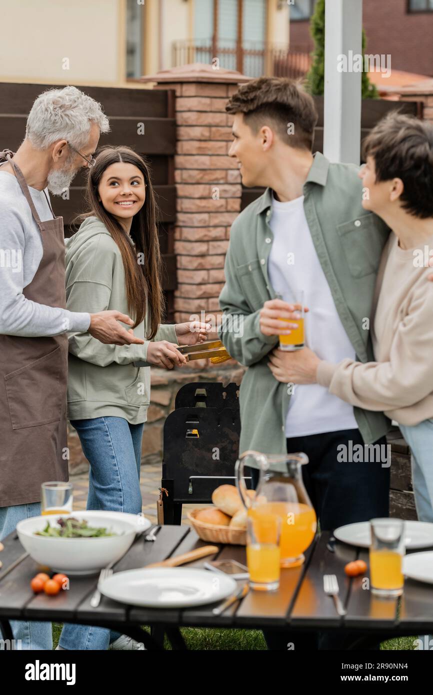 modern parenting, happy parents day, father and teenage daughter preparing food on bbq grill, mother hugging with cheerful young adult son holding gla Stock Photo