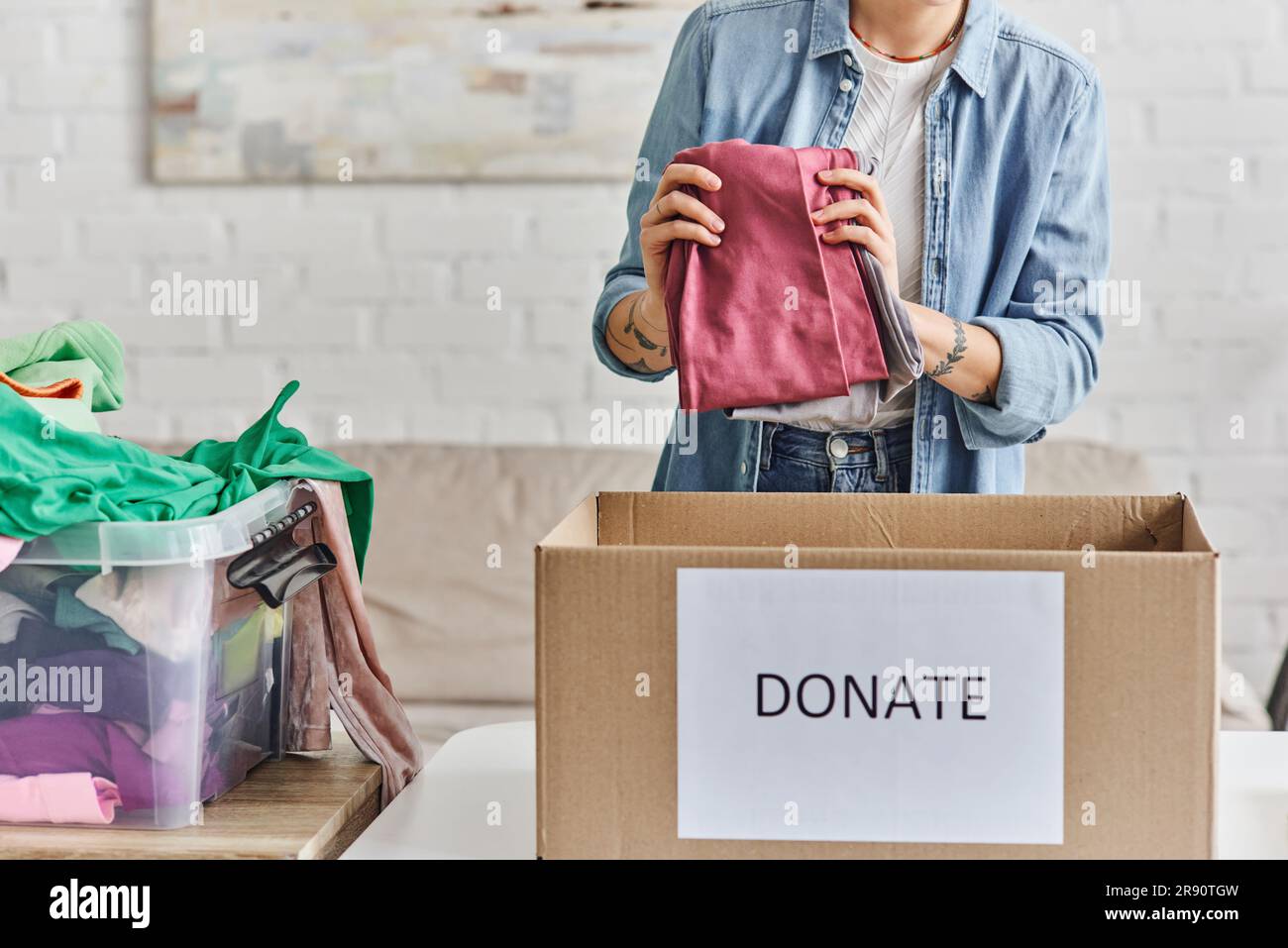 charity and volunteering, cropped view of young and tattooed woman holding  wardrobe garments near carton box with donate lettering, sustainable living  Stock Photo - Alamy
