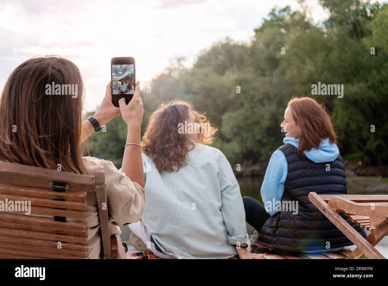 Women friends relaxing together outdoors in nature and taking photos using smart phone. Stock Photo