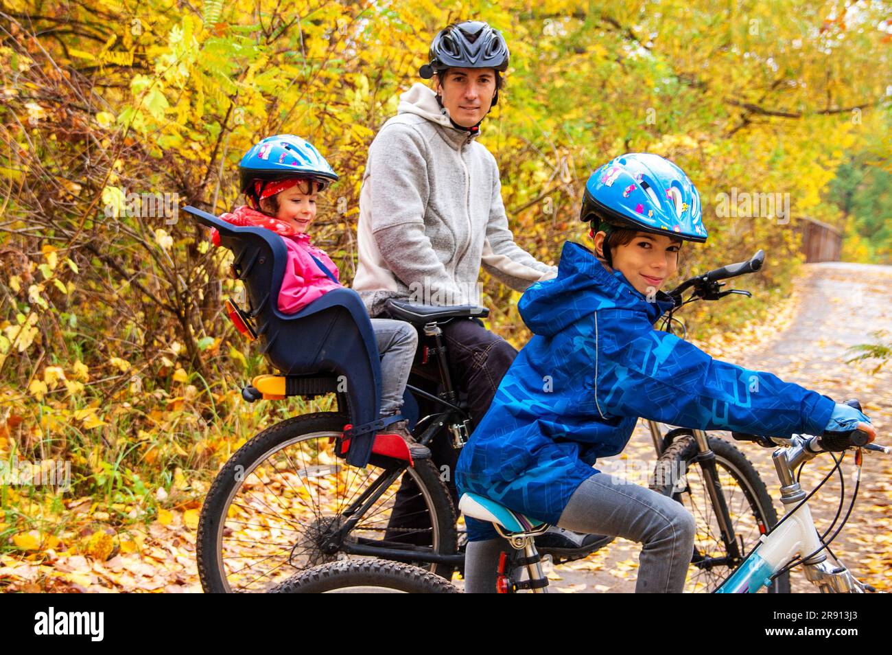 Family cycling in golden autumn park, active father and kids ride bikes, family sport and fitness with children outdoors Stock Photo