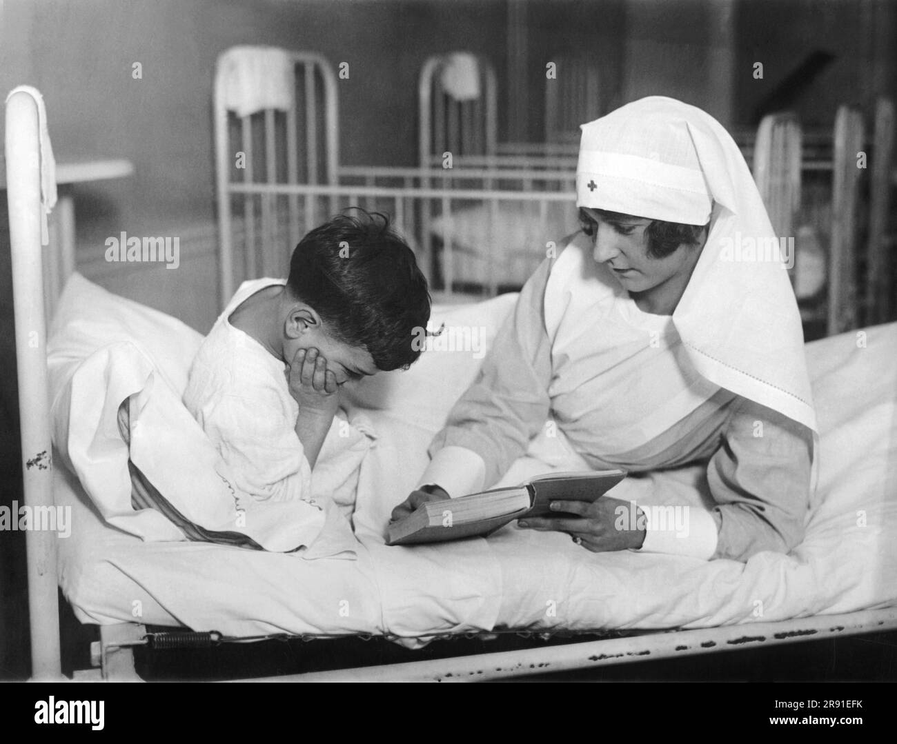 New York, New York:  January 5, 1926 New York City society girls are spending one day a week as volunteer nurses as part of their service to humanity. Miss Betty Nixon is seeing reading to a young boy at the Tonsil Hospital in Manhattan. Stock Photo