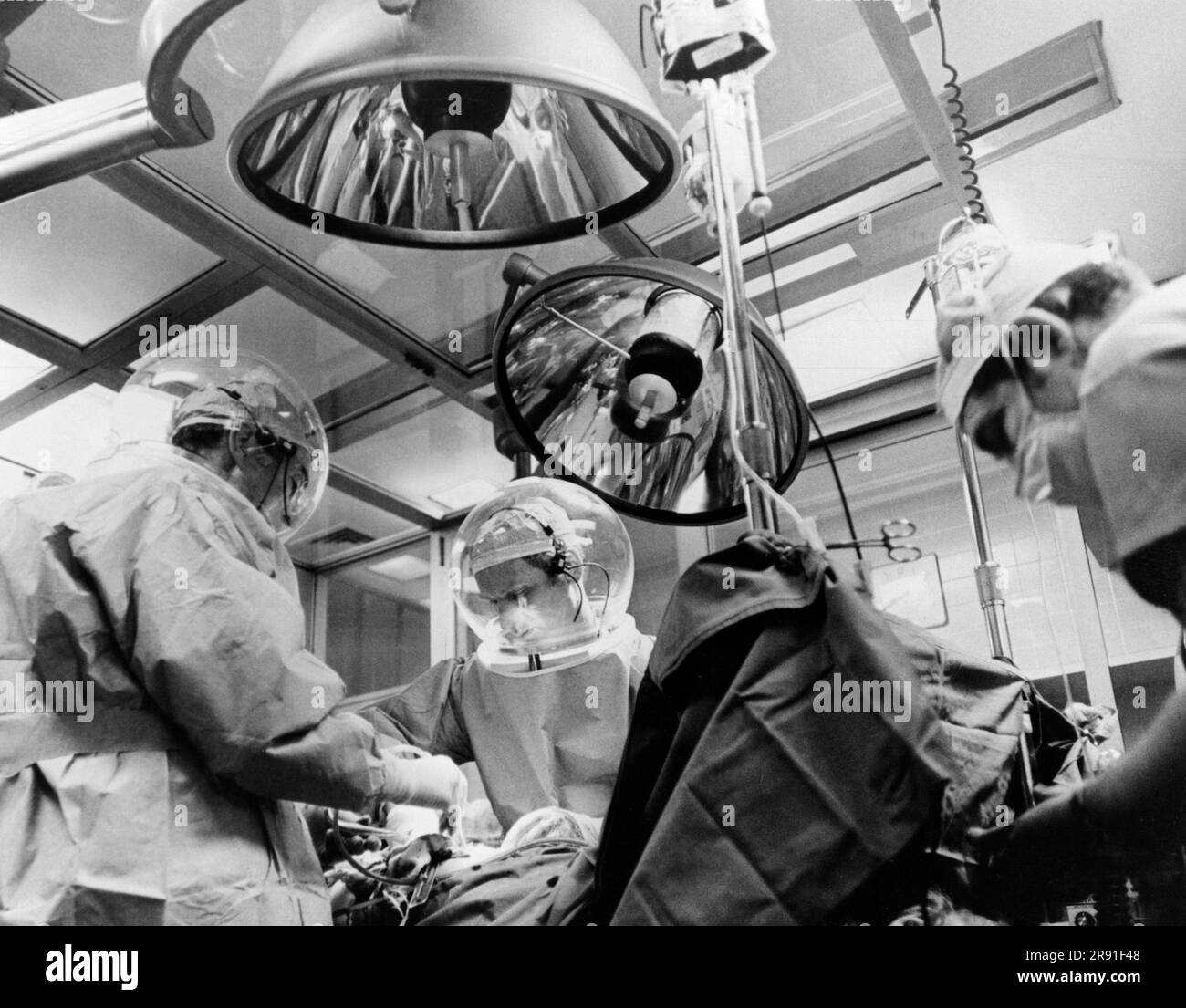 Denver, Colorado:  February 8, 1970 A surgery team at St. Luke's Hospital performing a hip joint replacement in a new clean room which helps lessen the danger of infection to the patient. It is being performed in a foldable clean roon which can be stored when not in use.  Air is forced in through the front and exits out the back and the operating team upwind of the patient wears astronaut type helmets and garments which are impermeable to bacteria. The clean room technique for surgery was developed by the Martin Marietta Corporation for NASA and is being tested at St. Luke's. Stock Photo