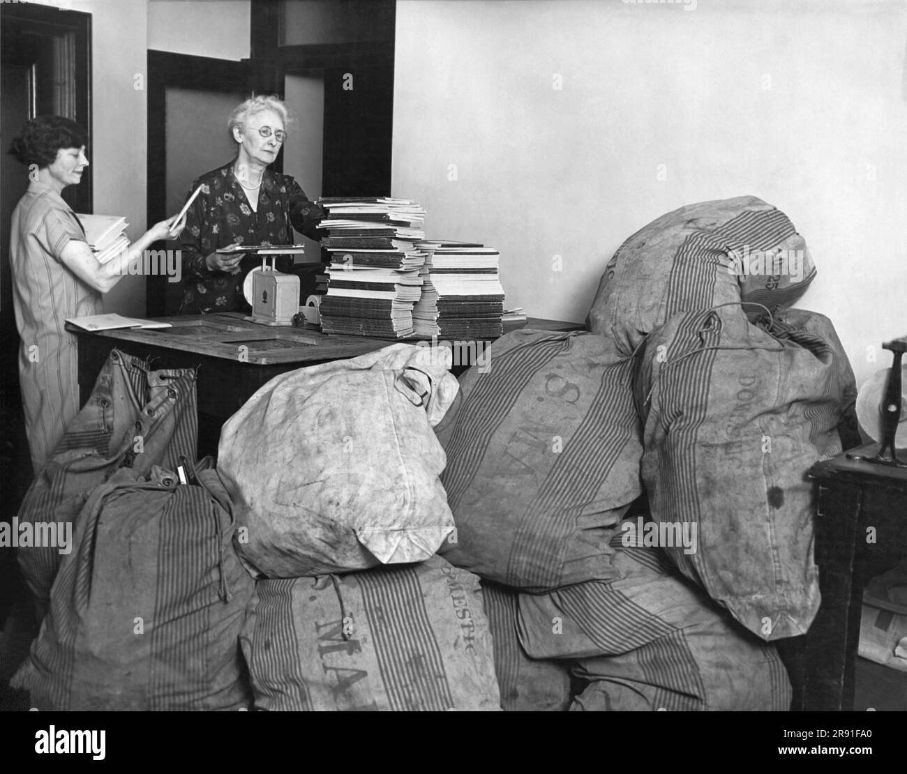 United States:  c. 1925 Two women in an office are overworked with mailings, and they have many more to go. Stock Photo