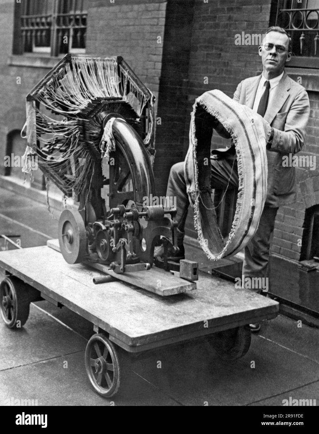 Washington, D.C.:  August 21, 1925. A Smithsonian Institute official holding the portable tire making device that was presented to them today. He's standing with the fabric weaving loom machine, and the second machine, which is not shown, constructs a three ply rubberized fabric. This machine makes it possible to set up small auto tire factories anywhere that's desired. Stock Photo