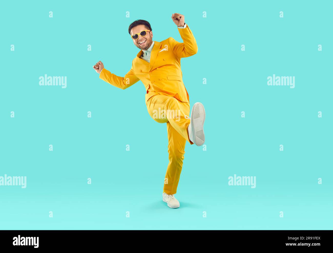 Happy, cheerful man in a yellow suit and sunglasses dancing on a blue