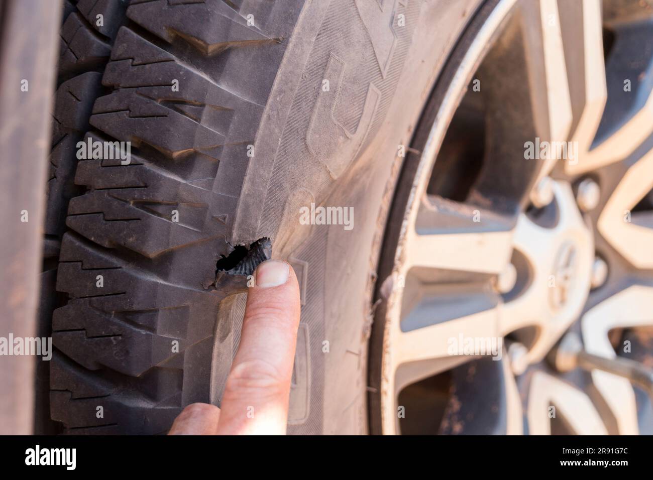 A hand shows a large hole in a car tyre on the rough dirt roads of Western Australia Stock Photo
