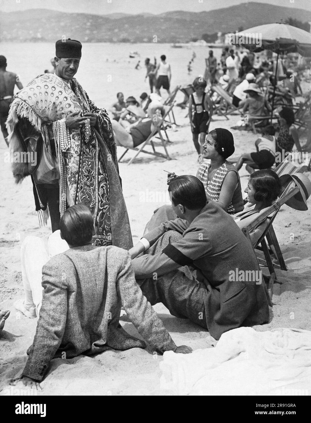 Nice, France:  1931 An Eastern vendor bargains with with a party of Americans on the beach at Nice. Stock Photo