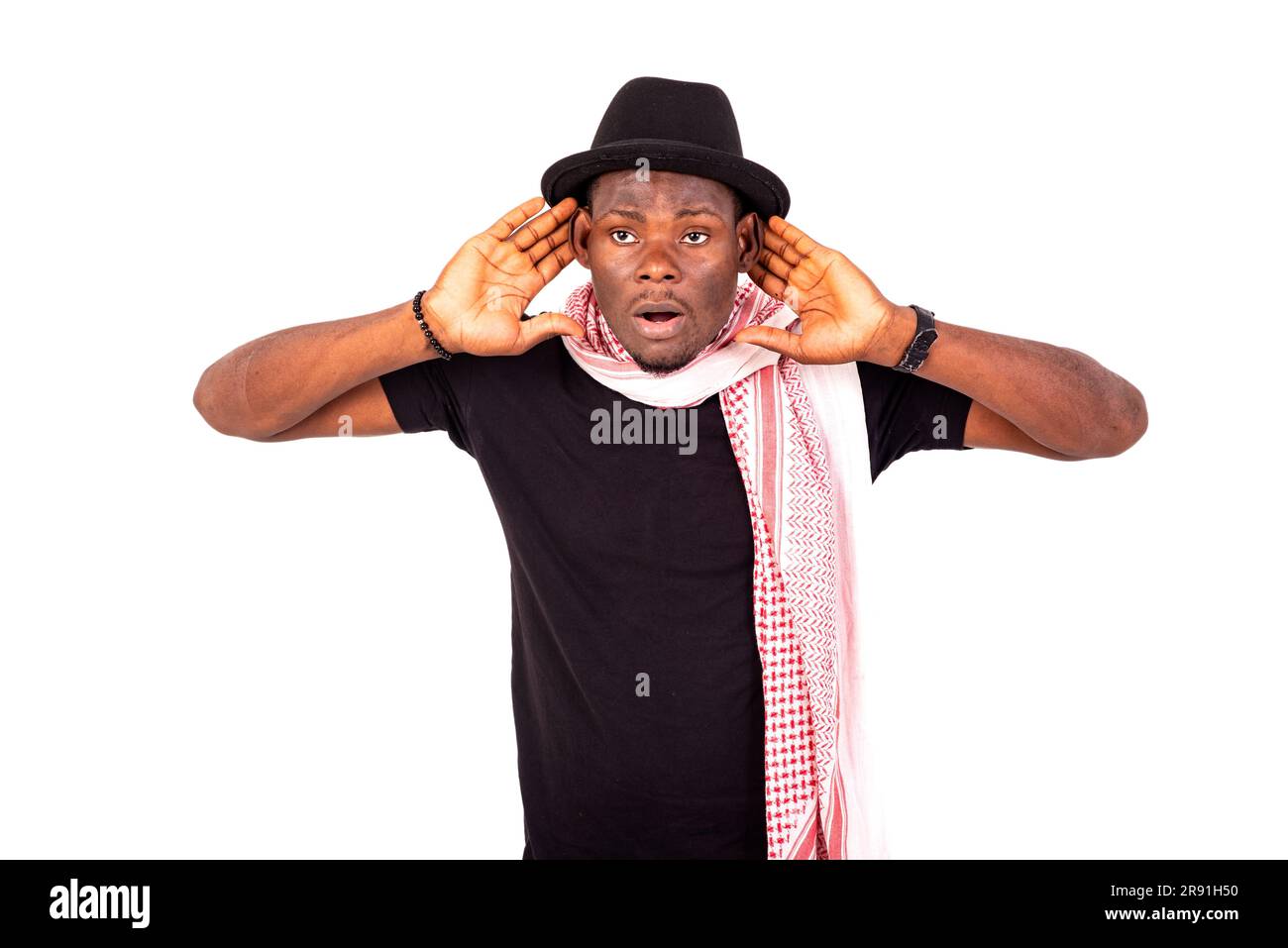 young man wearing a hat and scarf holding both hands on his ear for better listening. Stock Photo