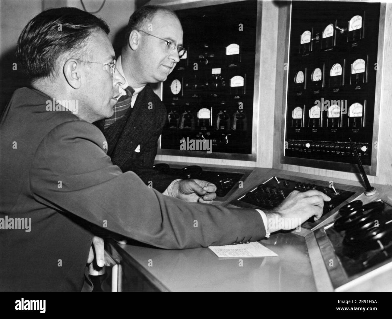 Berkeley, California, August 10, 1945 University of California's Dr. Ernest Lawrence, inventor of the cyclotron, and UC engineer WB Reynolds, examine the control panel of the 60 inch atom gun which is being used in the making of the first atomic bomb. Stock Photo