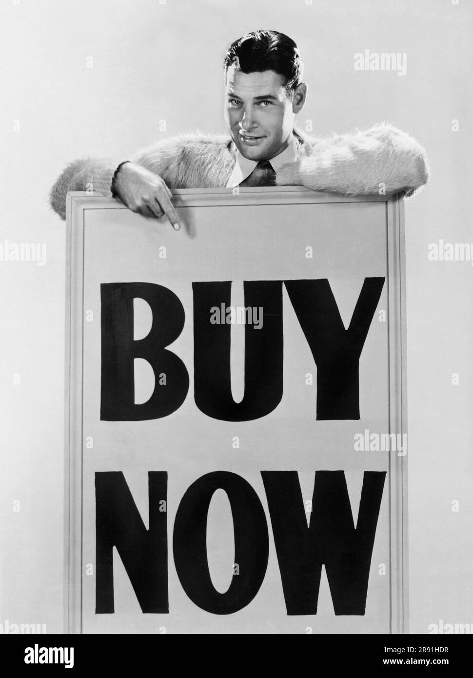 Hollywood, California:   c. 1930 Actor Richard Arlen believes that if money is kept in circulation, prosperity will return to the country. His slogan for good times is, 'Buy Now'. Stock Photo