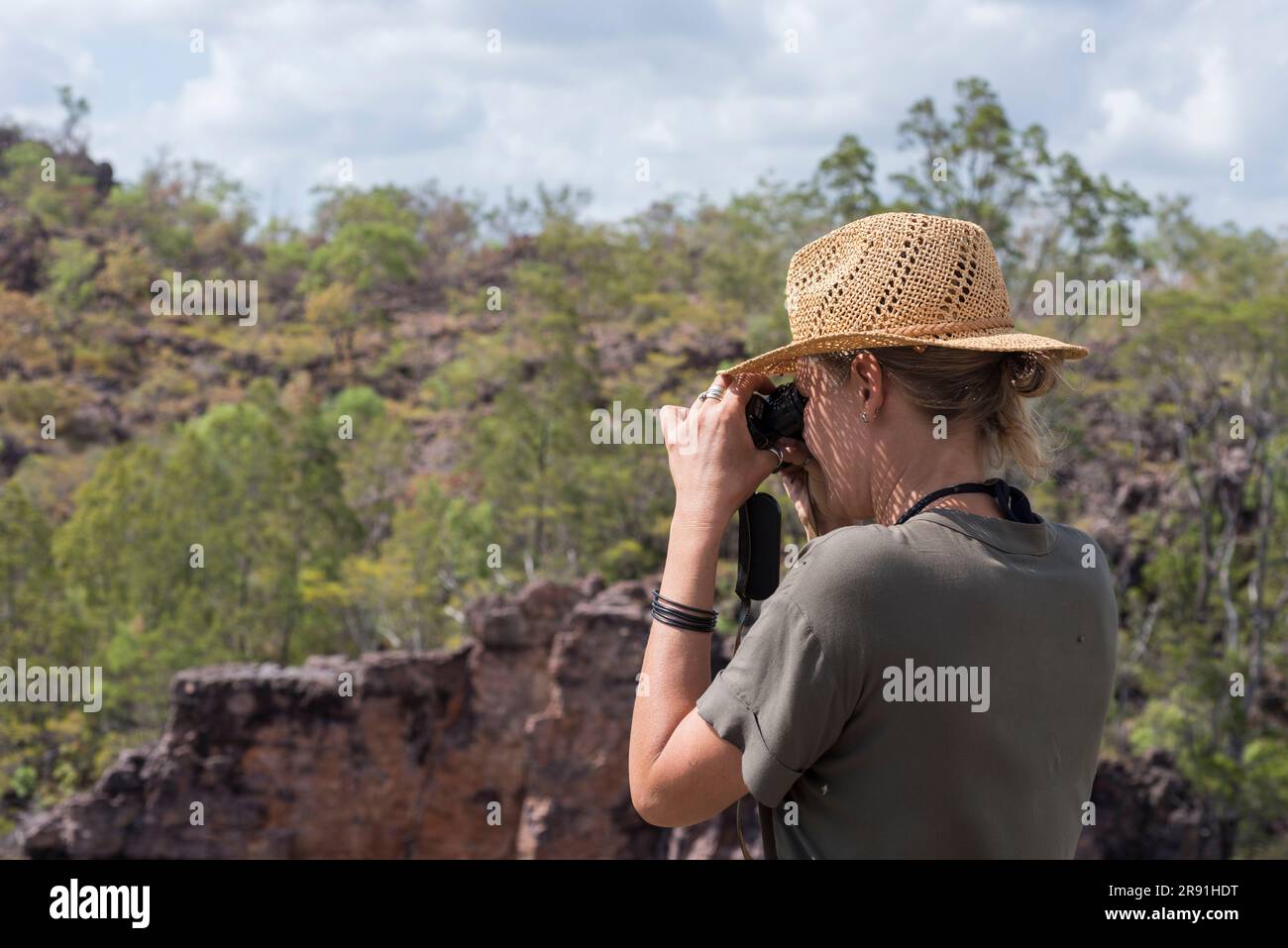 A woman in a sun hat looks at the view through a pair of binoculars near Jabiru in Kakadu National Park in Australia Stock Photo