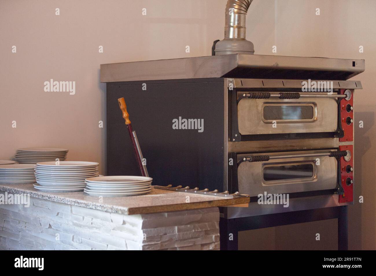 Pizza oven with on its side, a pizza peel and a counter fool of pizza plates. Stock Photo