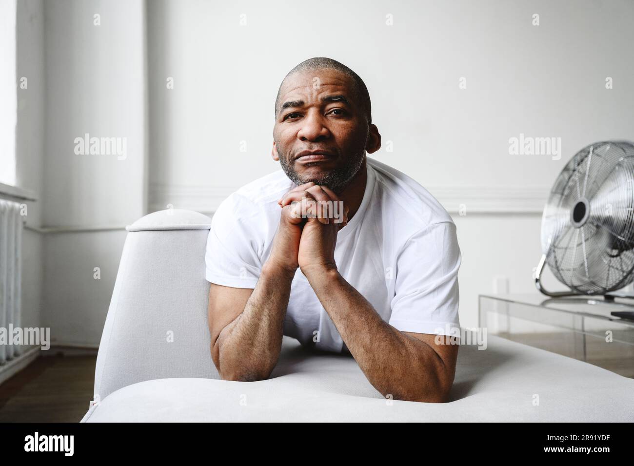 Mature man with hands clasped leaning on sofa at home Stock Photo