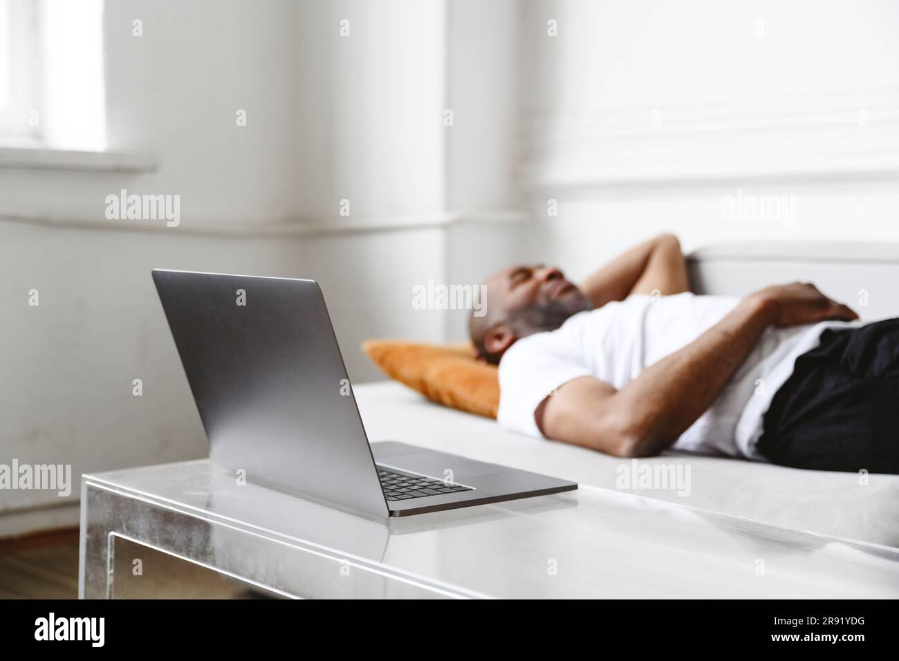 Laptop on table with freelancer lying on sofa in background Stock Photo