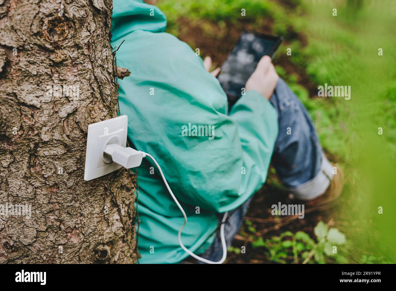 Man using tablet computer charging with outlet on tree trunk Stock Photo